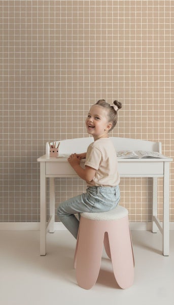 Kind sitzt an Schreibtisch vor Wandtapete mit quadratischem Muster