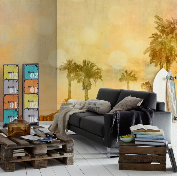Wohnzimmer im Industriestil mit Fototapete mit Palmen, dunklem Sofa, Couchtisch aus Paletten und Metallschrank mit bunten Schubladen.