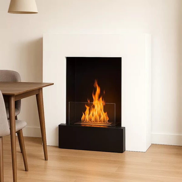 Moderner Bioethanol Kamin mit weißer Umrandung und brennender Flamme in einem hellen Wohnraum mit Holztisch.