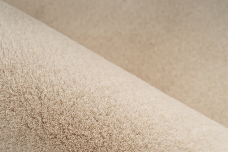 Nahaufnahme eines weichen, beigen Kunstfellteppichs mit dichter Florstruktur.