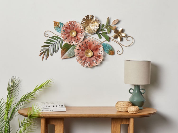 Wanddekoration aus Metall mit Blumenmotiven über einem Holztisch mit Lampe.