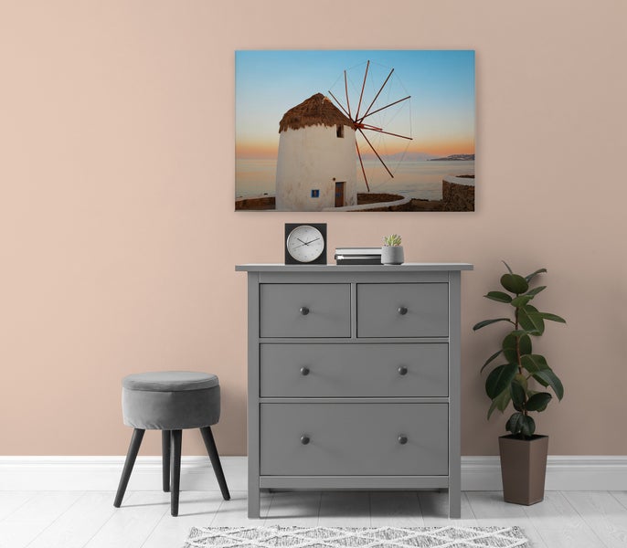 Wandbild mit einer Windmühle am Meer über einer grauen Kommode mit einem Hocker und einer Pflanze in einem modern eingerichteten Wohnraum