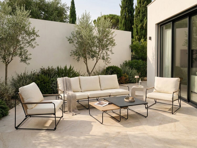 Helle Gartenszene mit einer Couch, zwei Sesseln und zwei Couchtischen vor einer Wand und Büschen