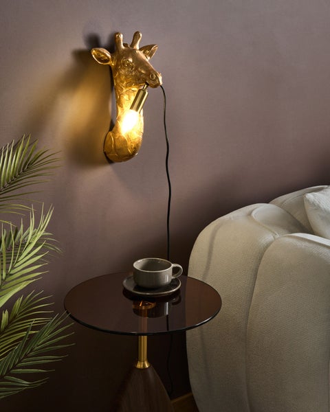 Wandleuchte in Form eines goldenen Giraffenkopfes neben einem Beistelltisch mit einer Tasse.