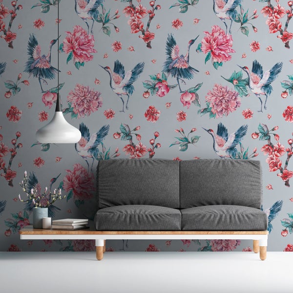 Vliestapete mit Kranich- und Blumenmuster in einem modernen Wohnzimmer mit grauem Sofa und weißer Pendelleuchte.