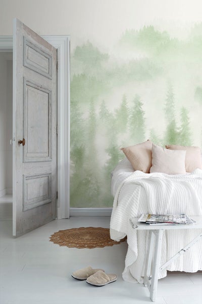 Schlafzimmer mit Bett vor einer Wandtapete mit Waldmuster, einem Holztisch mit Zeitschriften, einem runden Teppich und einer offenen Holztür.