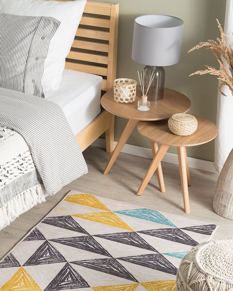 Helles Schlafzimmer mit Holzbett, gestreifter Bettwäsche, zwei runden Holzbeistelltischen und einem Teppich mit geometrischem Dreiecksmuster.