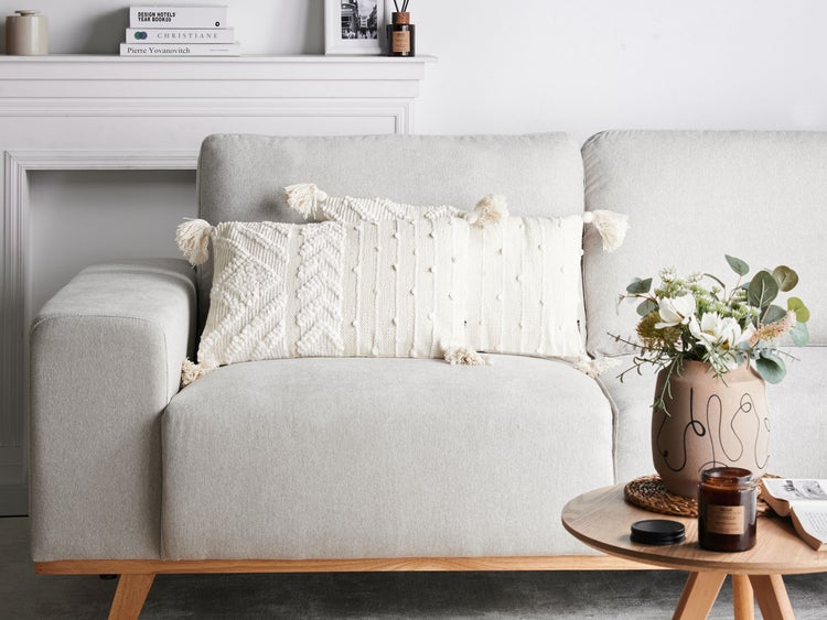 Wohnzimmer mit Sofa, Dekokissen mit Fransen und Beistelltisch mit Blumenvase