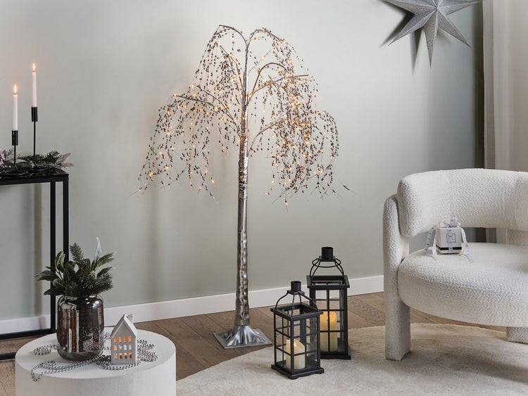 Dekoratives Wohnzimmer mit beleuchtetem Baum, Laternen, Sessel und dekorativen Elementen für eine festliche Atmosphäre.