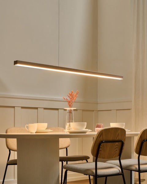 Modernes Esszimmer mit schmaler LED-Pendelleuchte über einem weißen ovalen Tisch, Holzstühlen und Keramikgeschirr in heller Atmosphäre.