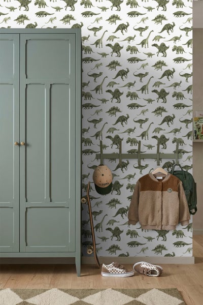 Kinderzimmer mit Vliestapete im Dinosaurier-Design, einem grünen Kleiderschrank aus Holz, einer Garderobe sowie einem Skateboard und Schuhen.