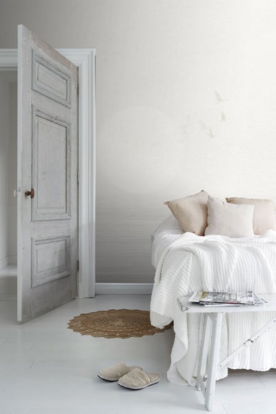 Helles Schlafzimmer mit Bett, Beistelltisch, Teppich, geöffneter Tür und Tapete mit Vogelmotiv