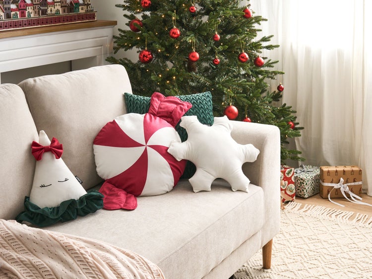 Weihnachtliche Wohnzimmerszene mit Sofa, Kissen in Form von Weihnachtsfiguren und geschmücktem Weihnachtsbaum