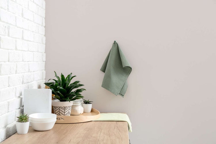 Gestreiftes Geschirrtuch hängend in einer hellen Küche mit Ziegelwand, Zimmerpflanzen und weißem Geschirr auf hölzerner Arbeitsplatte.