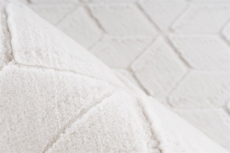 Nahaufnahme eines weißen weichen Teppichs mit geometrischem Rautenmuster.