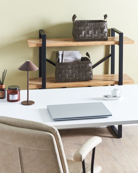 Moderner Arbeitsplatz mit weißem Schreibtisch, Laptop, Holzregal mit schwarzem Metallrahmen und dunkelbraunen geflochtenen Aufbewahrungskörben.