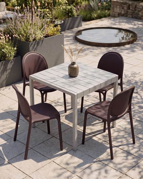 Modernes Gartenmöbel-Set mit quadratischem Gartentisch und vier Stühlen auf einer gepflasterten Terrasse mit Pflanzkübeln im Hintergrund.