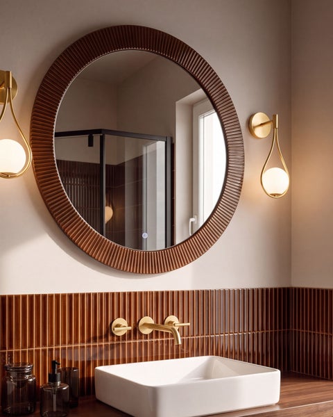 Helles Badezimmer mit rundem Spiegel, Aufsatzwaschbecken, goldener Wandarmatur und vertikalen braunen Fliesen.