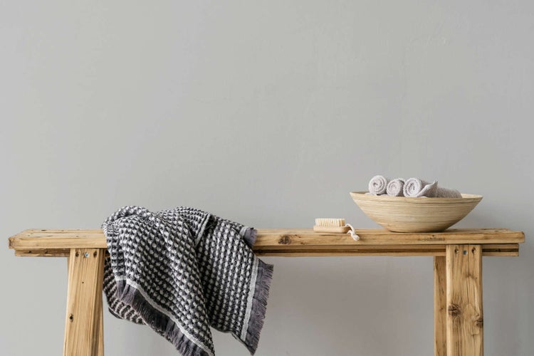 Rustikale Holzsitzbank mit einem gemusterten Handtuch, einer Holzschale mit Gästetüchern und einer Nagelbürste.