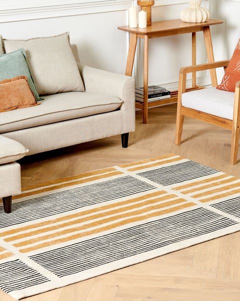 Wohnzimmer mit Sofa, Sessel, Holztisch und einem Teppich mit Streifenmuster.