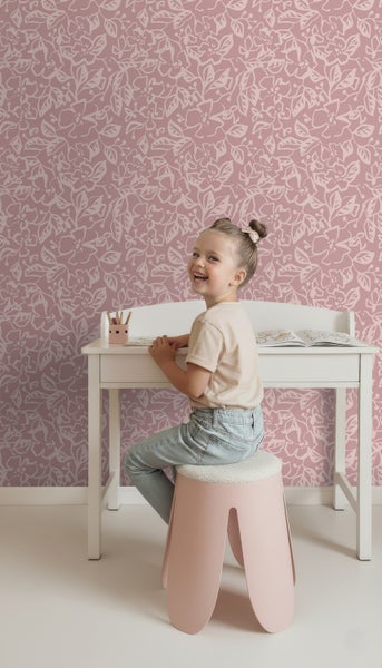 Mädchen sitzt an einem weißen Kinderschreibtisch vor einer rosafarbenen Blümchentapete