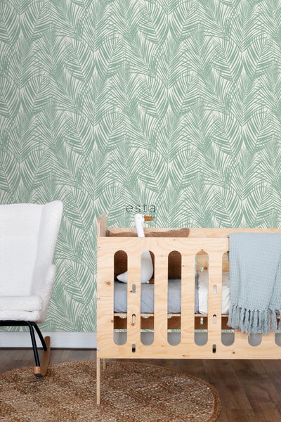 Ein Kinderzimmer mit einer Wandtapete mit Blattmuster, einem Kinderbett aus Holz und einem Schaukelstuhl