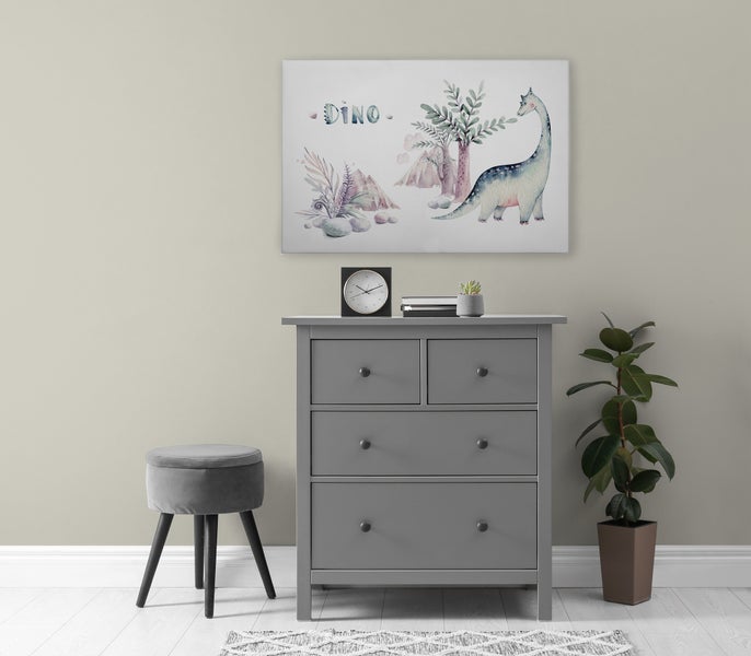 Graue Kommode mit vier Schubladen, darüber ein Wandbild mit Dino Motiv, daneben ein Hocker, eine Pflanze und ein Wecker.