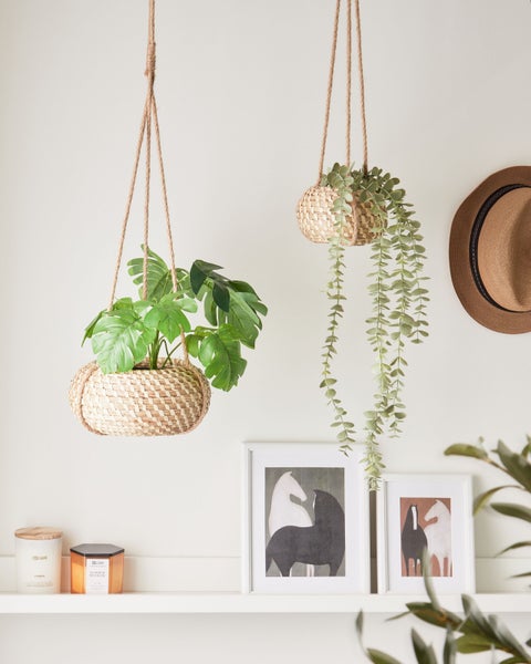 Dekorative Szene mit hängenden Pflanzenkörben, Regalen, Kerzen, Bildern und einem Hut für ein gemütliches Ambiente