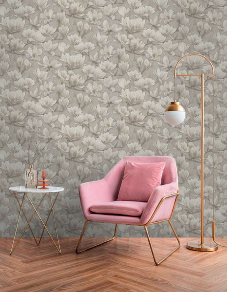 Wohnzimmer mit Vliestapete mit Magnolienmuster, einem pinken Samtsessel, einem runden Beistelltisch und einer Stehlampe auf einem Holzfußboden.
