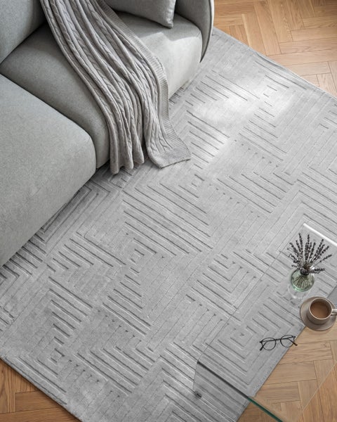 Wohnzimmer mit Teppich mit geometrischem Muster vor einem Sofa mit Decke auf einem Parkettboden.