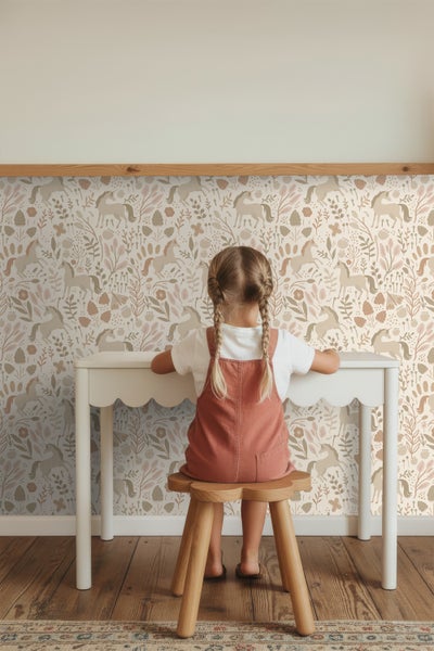 Mädchen sitzt an weißem Schreibtisch vor Tapete mit Pferdemotiv