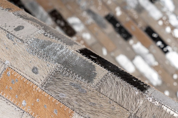 Patchwork-Teppich aus Kuhfell mit Zickzack-Nähten und silberfarbenen Metallic-Akzenten in der Nahaufnahme.