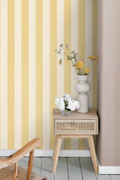 Gestreifte Vliestapete in einem hellen Zimmer mit Nachttisch aus Holz und dekorativen Vasen mit Blumen.