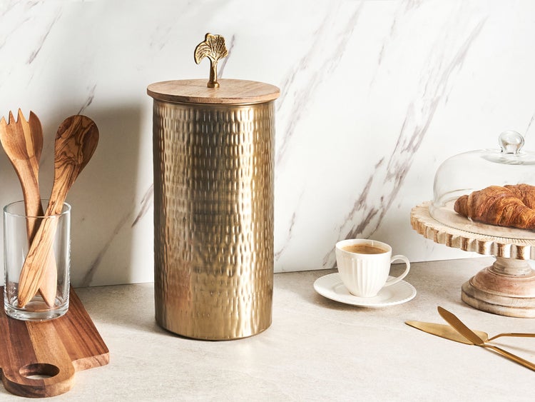 Zylindrische Vorratsdose aus gehämmertem Metall mit Holzdeckel und Ginkgoblatt-Griff in einer hellen, modern organisierten Küchenumgebung.