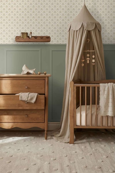 Gemütliches Kinderzimmer mit hölzerner Kommode und Kinderbett, dekoriert mit Betthimmel, Wandregal, Mustertapete und Strukturteppich.
