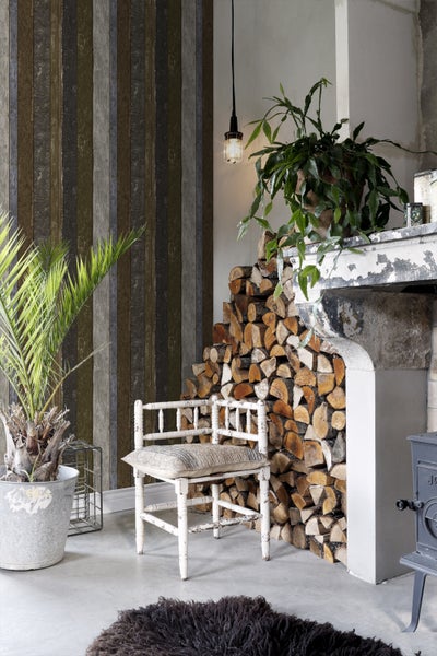 Gemütliches Wohnzimmer mit Holzwand, Kaminholz, Sessel und Zimmerpflanzen