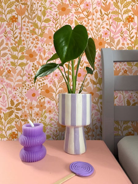 Dekorative Szene mit Zimmerpflanze in gestreiftem Topf, gewundener Kerze und floraler Tapete