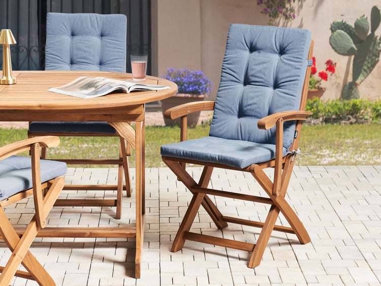 Hölzernes Gartenmöbel-Set mit rundem Esstisch und klappbaren Gartenstühlen inklusive Sitzkissen auf einer gepflasterten Terrasse im Garten.