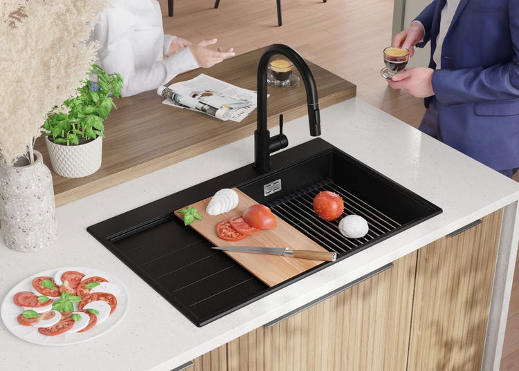 Küchenszene mit schwarzer Spüle, Armatur, Schneidebrett mit Lebensmitteln und Personen im Hintergrund