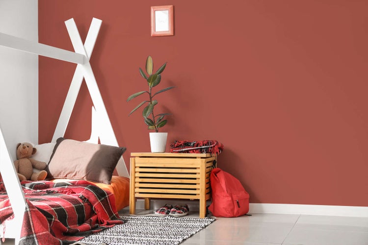 Kinderzimmer mit terrakottafarbener Wand, einem weißen Tipi-Bett aus Holz und einem hölzernen Nachtkästchen mit einer Zimmerpflanze.