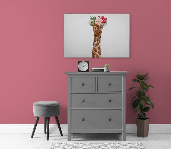 Eine Kommode aus Holz mit einer Giraffe als Leinwandbild an der Wand, einem Hocker und einer Pflanze in einem hellen Raum.