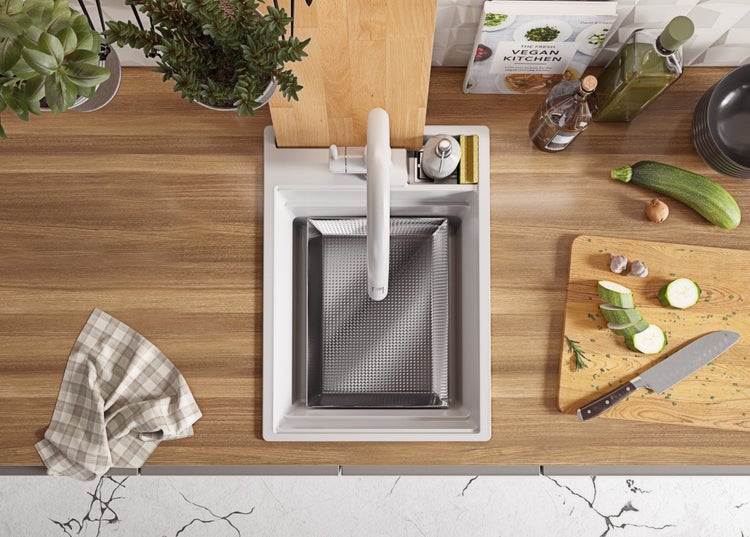 Ansicht von oben auf eine Küchenspüle mit Armatur, Spülmittelspender, Schneidebrett, Gemüse, Kräutern und Kochbuch