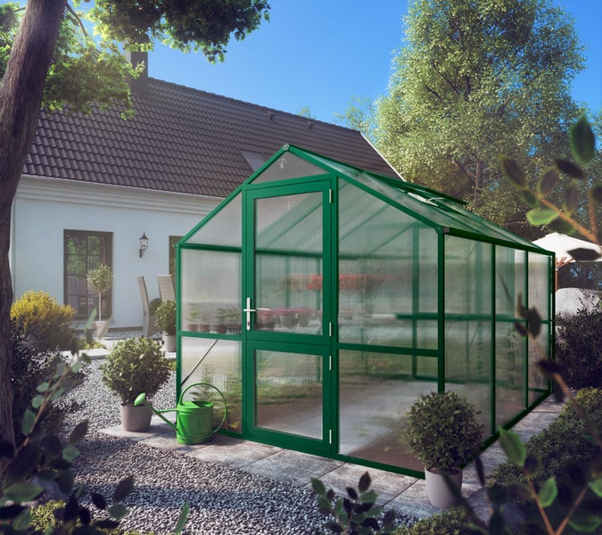 Gewächshaus mit Aluminiumrahmen und Hohlkammerplatten in einem Garten mit Pflanzen und Kiesweg vor einem Wohnhaus.