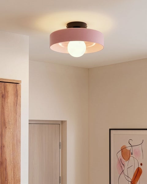 Moderne Deckenleuchte mit rosa Schirm und weißem Glaskolben in einem hellen Raum mit Holzschrank und Wandbild.