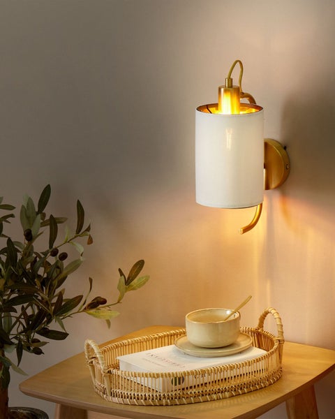 Wandleuchte aus Stoff mit goldfarbenen Akzenten über einem Tisch mit Dekoration.