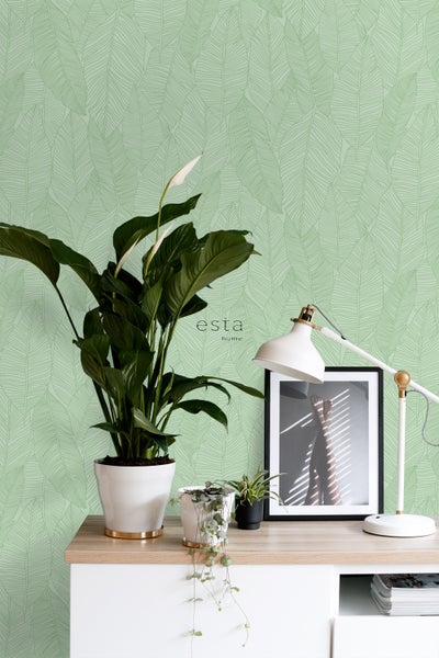 Dekoratives Zimmer mit einer Wandtapete mit Blattmuster, einem Schreibtisch, einer Lampe und Zimmerpflanzen für ein helles Ambiente.