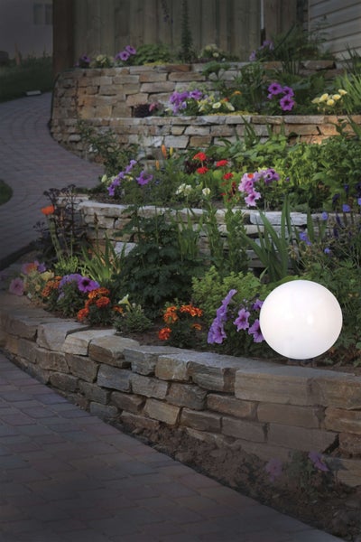 Szene mit Garten, Steinmauer, Blumen und runder Leuchte