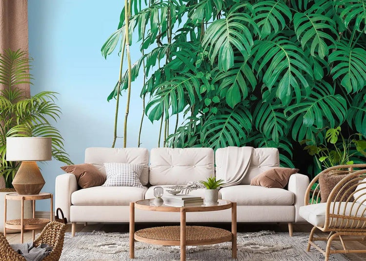 Hell eingerichtetes Wohnzimmer mit einer Fototapete mit tropischen Monstera-Blättern, beige gepolstertem Sofa und rundem Holztisch.