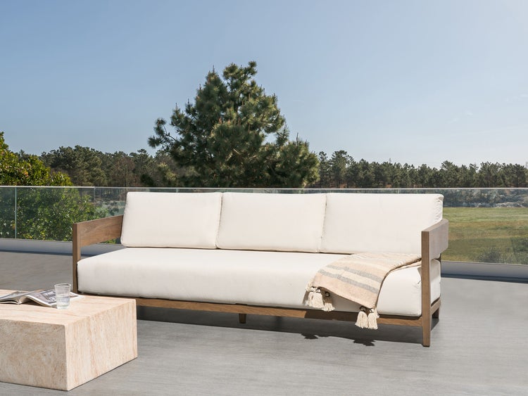Drei-Sitzer Gartensofa aus Holz mit hellen Auflagen und einer Decke auf einer Terrasse