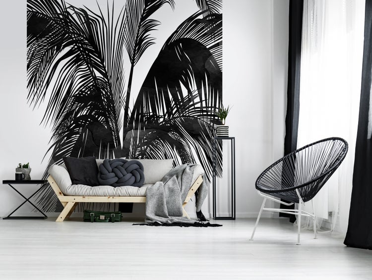 Modernes Wohnzimmer mit großflächiger Fototapete mit schwarzem Palmenblattmotiv, Holzsofa mit Kissen und schwarzem Acapulco Sessel.